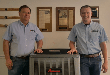 Employees in company uniforms showcasing an HVAC unit