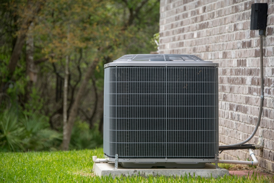Outdoor AC unit placed on stone base amidst green grass and trees